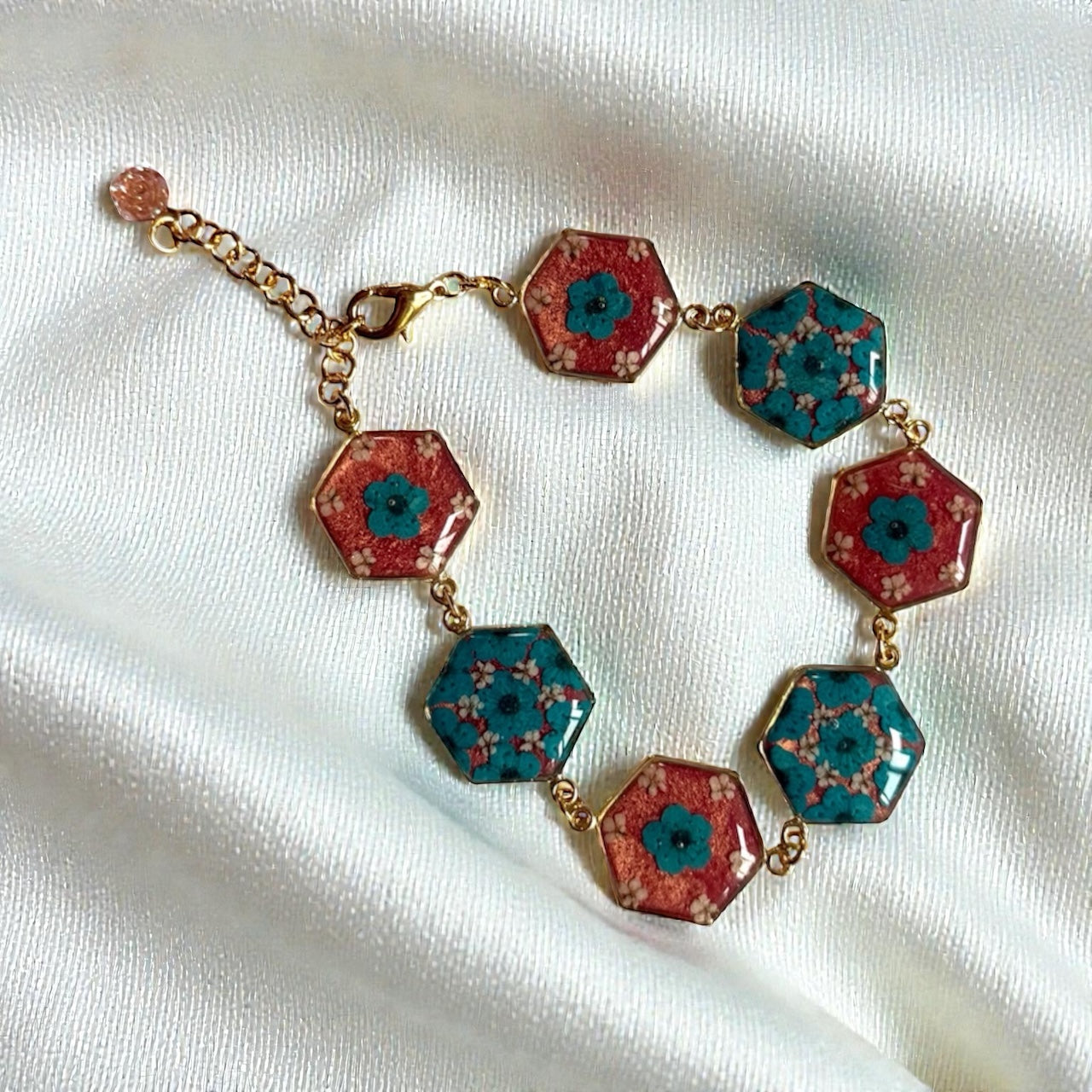 Gold Colored Bracelet with Teal Plum Blossoms, pieces of Queen Anne’s Lace in a Coral Pink Background